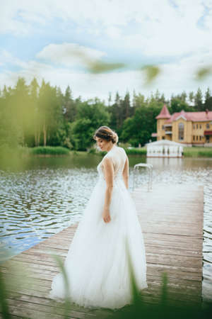 Portrait of a young beautiful bride on a background of a gorgeous view of the river and fields. Wedding day.の写真素材