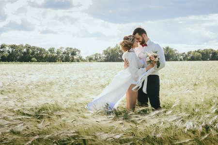 bearded groom and beautiful bride walking in the field at sunsetの写真素材