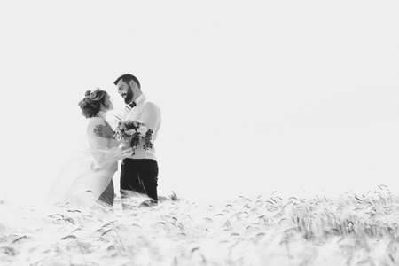 bearded groom and beautiful bride walking in the field at sunsetの写真素材
