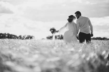 bearded groom and beautiful bride walking in the field at sunsetの写真素材