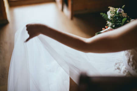 Fashion photo of a beautiful bride with flowers bouquet in her hands at the light room next to the doorsの写真素材