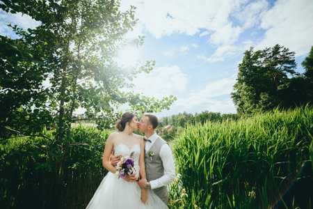 Stylish couple of happy newlyweds posing in the park on their wedding dayの写真素材