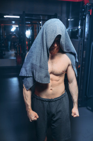 Smiling Indian athlete in sportswear standing with towel over his shoulder and posing for...