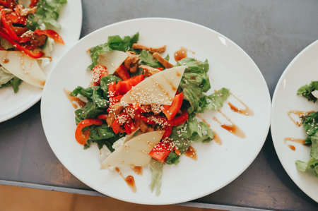 Green salad made with arugula, tomatoes, cheese mozzarella balls and sesame on plate, on color wooden backgroundの写真素材