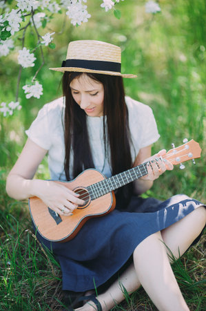 a beautiful girl in a straw hat plays a ukulele in a blossoming Apple orchardの写真素材