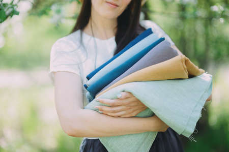 cropped image of smiling seamstress holding stack of colored fabricの写真素材