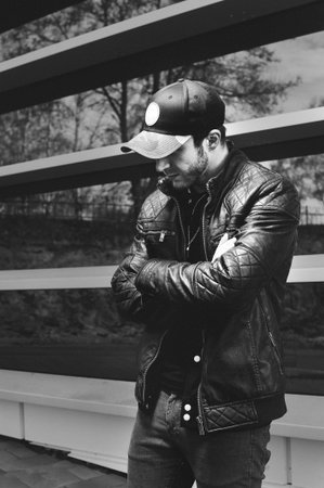 young man in a black fashionable baseball cap and black leather jacket posing on the street