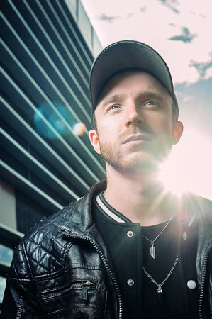 young man in a black fashionable baseball cap and black leather jacket posing on the street