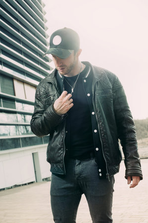 young man in a black fashionable baseball cap and black leather jacket posing on the street