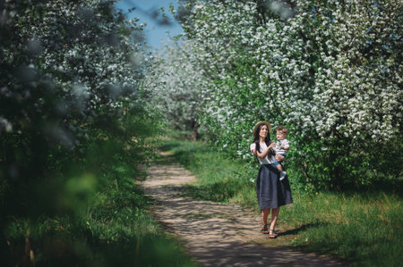 Little baby boy with her young mother in the blossom garden