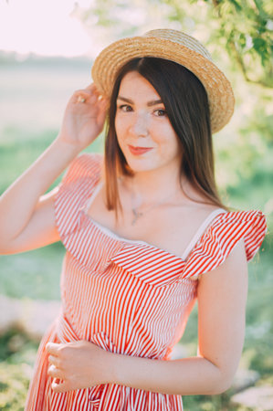 beautiful girl in a hat and red dress posing in nature. sunset