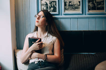 Stylish young hipster woman with notepad in cafe. Writes and ponders new ideas.の写真素材