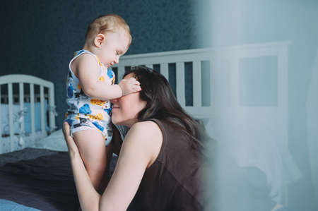 Young woman and little boy having fun in bed. one year oldの写真素材