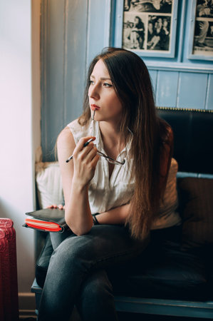 Stylish young hipster woman with notepad in cafe. Writes and ponders new ideas.