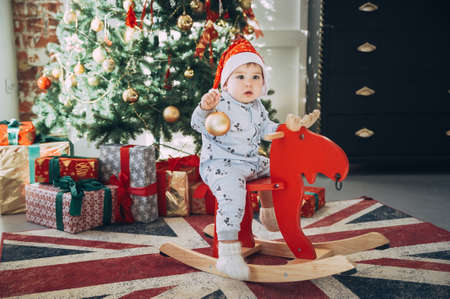 little baby boy in a Christmas cap sitting on a wooden horse by the Christmas treeの写真素材