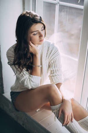 beautiful thoughtful girl sitting on the window in the studioの写真素材