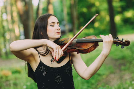 Beautiful girl in a black dress plays the violin in the woodsの写真素材