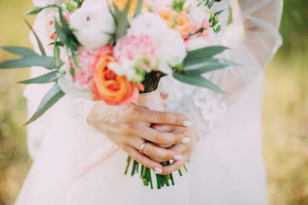 beautiful bouquet of different colors in the hands of the bride in a white dressの写真素材