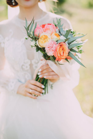 beautiful bouquet of different colors in the hands of the bride in a white dressの写真素材