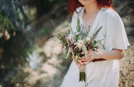 beautiful bride with red hair with a bouquet of wildflowersの写真素材
