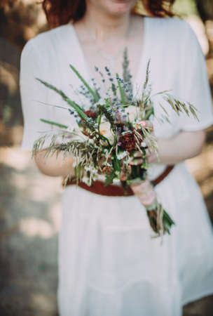 beautiful bride with red hair with a bouquet of wildflowersの写真素材