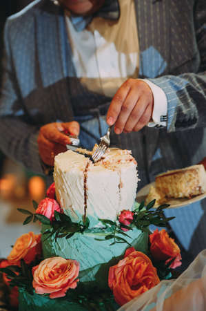 groom cuts a wedding cake. beautiful wedding cake in blue with red flowersの写真素材