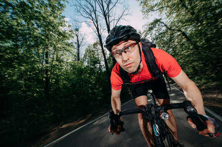 a professional cyclist in a helmet rides fast along a forest roadの写真素材