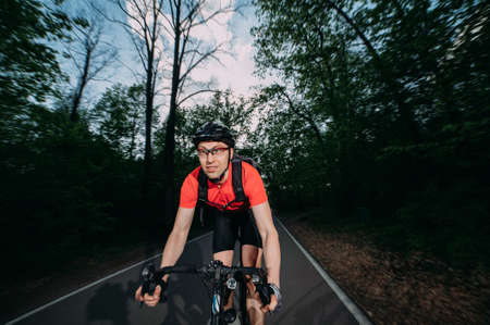 a professional cyclist in a helmet rides fast along a forest roadの写真素材