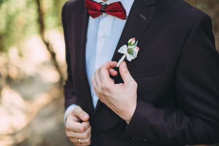the groom in a suit adjusts the bouton Floral traditional decoration for groom, an accessory on festive wedding suit. Close-upの写真素材