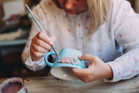 Woman working In her pottery studio. Ceramic workshop. Paint on clay mug in the pottery.の写真素材