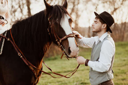 handsome groom in a hat stroking a horse. man with a horseの写真素材