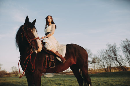 Beautiful stylish bride sits on a horse and looks into the distance. Evening timeの写真素材