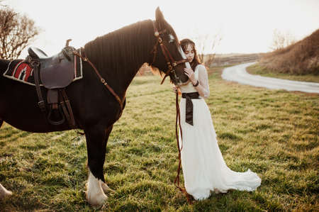 The young beautiful bride in a dress laid a hand on the head of a lashadi. Sunset photoの写真素材