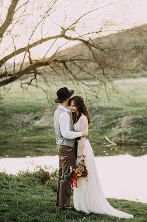 Wedding couple walking on bridge near lake on sunset at wedding day. Bride and groom in loveの写真素材