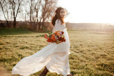 the bride is spinning in a light flying dress at sunset. focus on the wedding bouquetの写真素材
