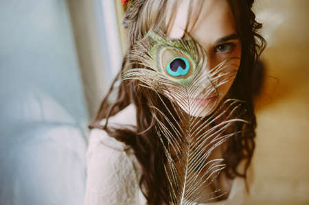 bride in a wedding dress looks at the camera. holding a peacock featherの写真素材