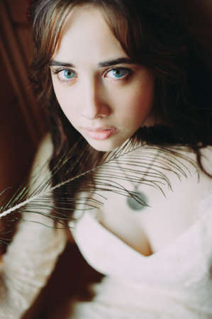 bride in a wedding dress looks at the camera. holding a peacock featherの写真素材