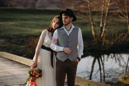bride and groom on the background of the river. bride with a bouquet. the groom in the hat. rustic style. bohoの写真素材