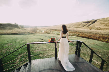 beautiful young bride in a beautiful dress stands on a wooden bridge against the background of the river. flowers in the hair. boho styleの写真素材