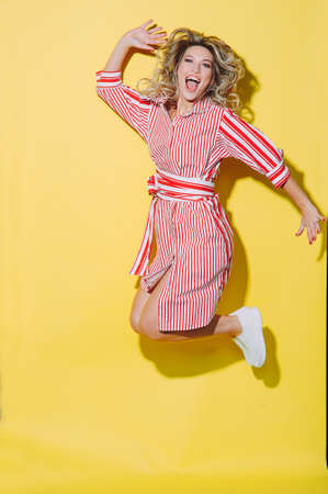concept happy emotional young woman in red summer dress and hat jumping and laughing on yellow backgroundの写真素材