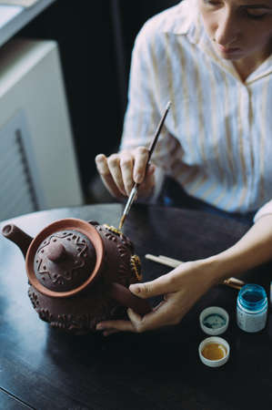 woman master paints the dishes at the workshop. clay teapot. handwork. Studio. designの写真素材