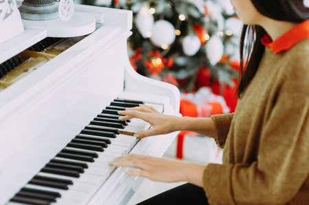 Brunette plays on a white piano against the background of a Christmas tree. Hands close-upの写真素材
