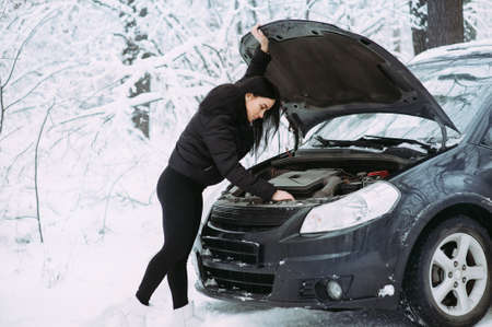 beautiful girl near the motor of a broken car on a winter snowy road. calls for helpの写真素材