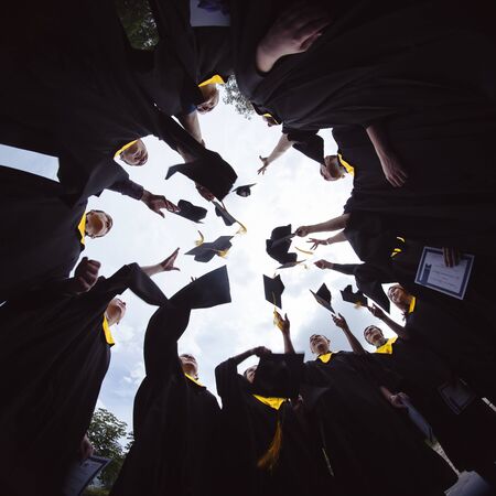 MOSCOW. RUSSIA, 06.11.2015: Congratulations Low angle view of happy group of graduates in black gowns, throwing up their head wear in the air and celebrating, in blue summer sky, laughing, enjoyingのeditorial素材