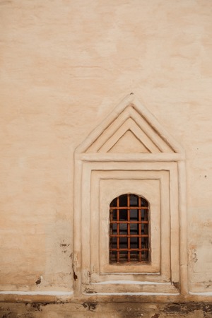 Old yellow wall with closed window with old rusty iron grid frontの写真素材