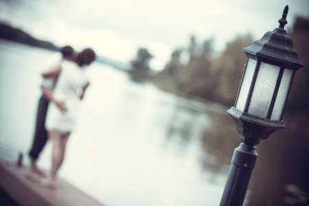 Guy and girl stand embracing on the river bank near the black lantern in the old styleの写真素材