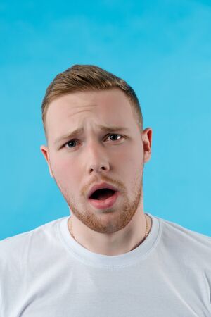 White man with open mouth on a blue background. The man has a surprised face. Fashionable man with a short haircut.の写真素材