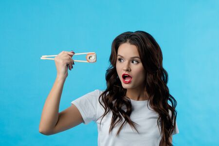 The beautiful brunette girl opened her mouth in surprise. Girl shows emotions she holds hashi with wooden chopsticks sushi. Lady with a cool haircut. The concept of beauty, fashion, advertising.の写真素材