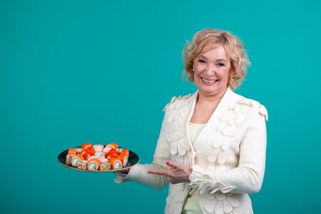 Satisfied lady shows her hand points to a large set of sushi. Lady on a green background. The concept of food, beauty, restaurant, studio, fashion.の写真素材
