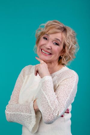 Kind grandmother with a short curly haircut, very cute smiles at the camera. She is wearing a white jacket. The concept of the model, advertising, beauty, emotions, fashionの写真素材